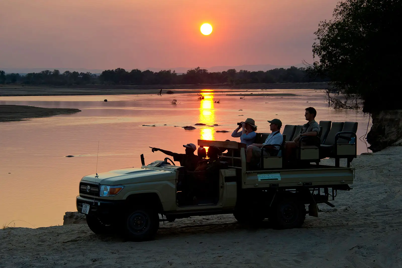 Guests in an open safari vehicle watching the sun set over the Luangwa River